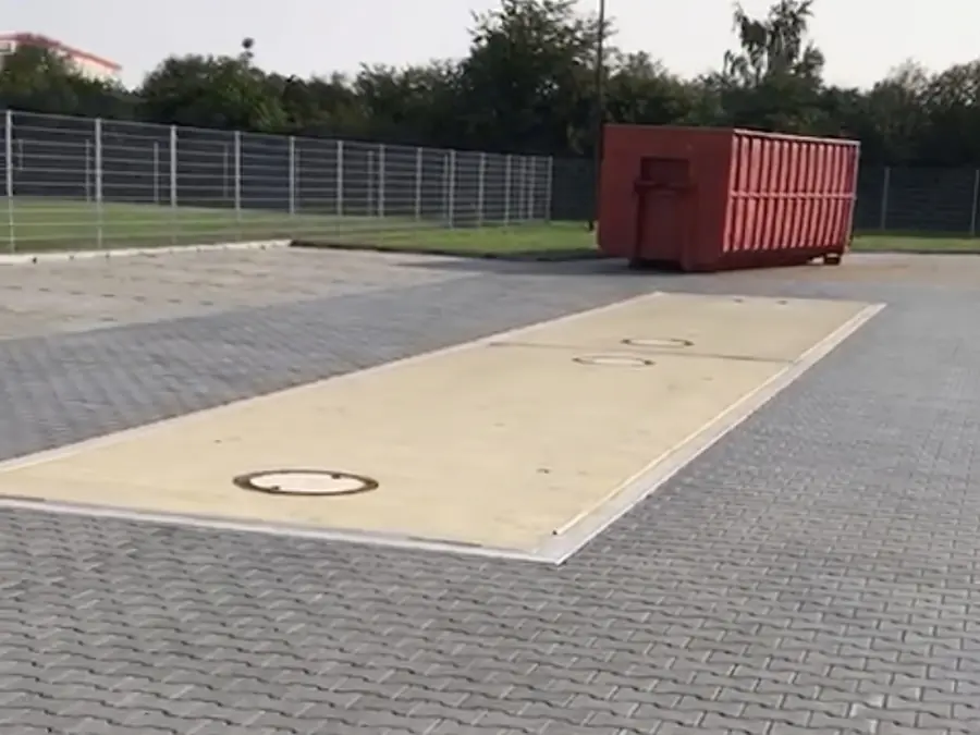 Geeichte Fahrzeugwaage im Hof am Standort Leipzig: die bodengleiche Wiegebrücke, dahinter ein Abrollcontainer.